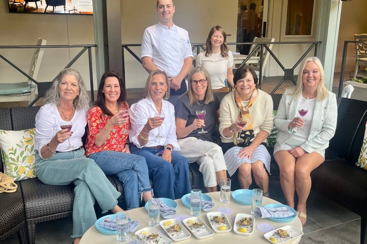 Group of people sitting outdoors, holding drinks, smiling at the camera.