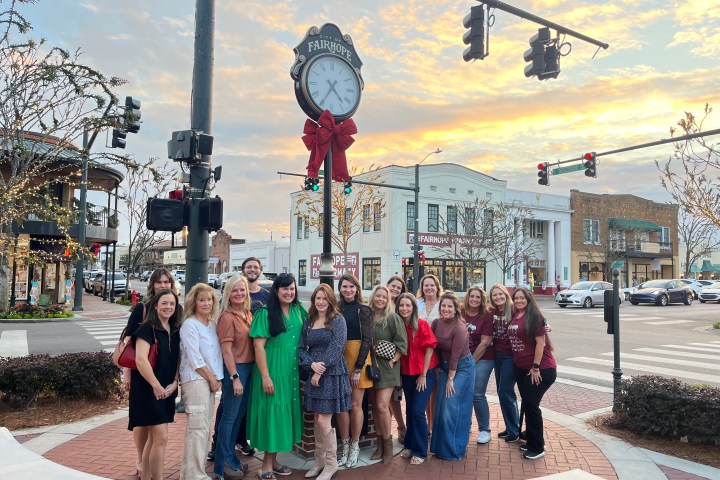 Group of people posing by a street clock with festive bow at sunset in a town square.