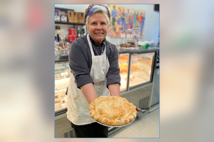Person in apron holding a freshly baked pie indoors.